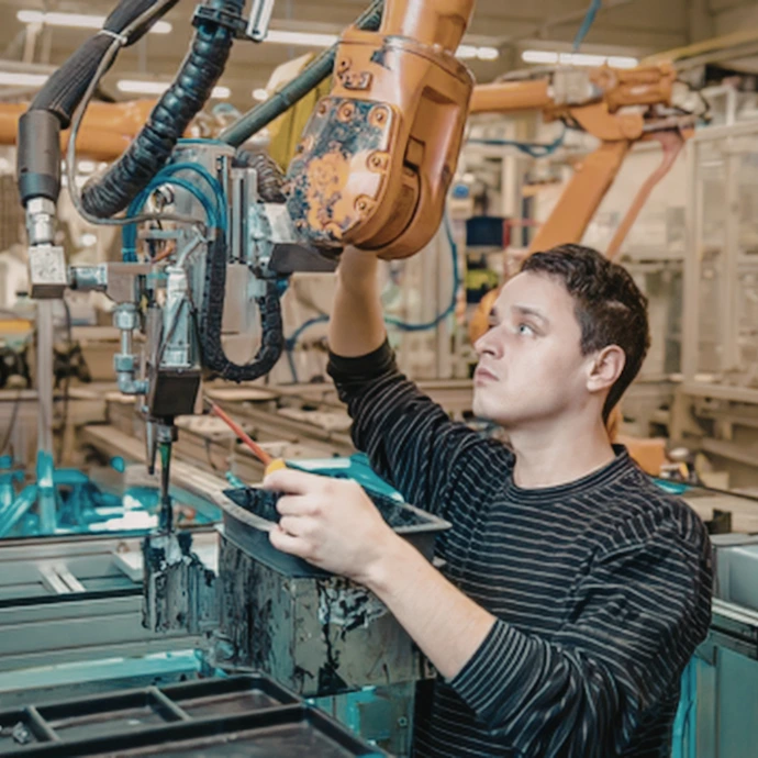 Gros plan sur un technicien qualifié en train de régler et de superviser une ligne de production automatisée dotée d'un bras robotique dans un atelier industriel. Idéal pour illustrer l'industrie 4.0, l'automatisation des procédés et la maintenance de machines.