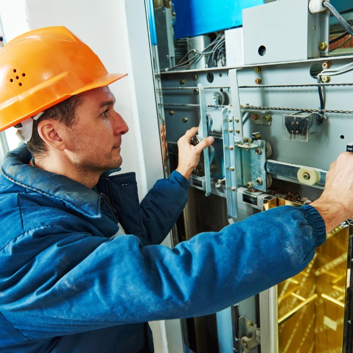 Gros plan sur un technicien qualifié portant une tenue bleue et un casque de chantier orange, en train d'inspecter et d'entretenir les mécanismes d'un équipement industriel complexe. Idéal pour les secteurs de la maintenance, de la mécanique et de la sécurité en usine.
