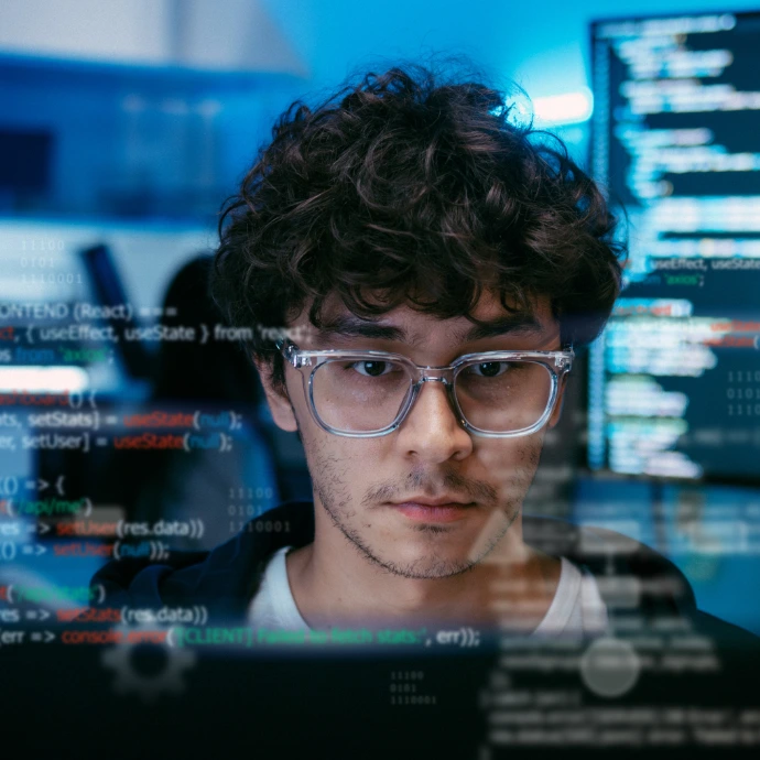 Portrait rapproché d'un jeune homme portant des lunettes, concentré sur son travail de programmation, avec des lignes de code et des interfaces logicielles en surimpression sur l'écran. Parfait pour les métiers du numérique, le développement web et l'ingénierie logicielle.